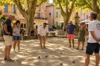 pétanque players chatting around a cochonnet on a sunny Provençal square under plane trees