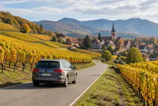 Route traversant les vignobles alsaciens avec un village à colombages et les Vosges en arrière-plan.